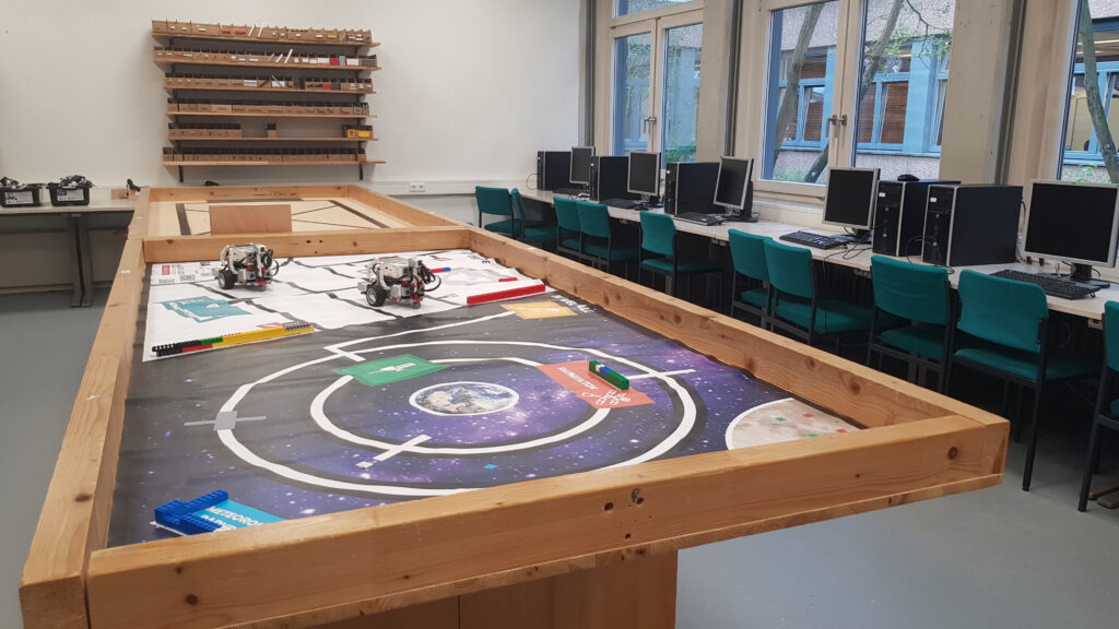 Zwei Tische mit Rand auf denen Lego-Roboter stehen. Rechts daneben Computer zum Programmieren der Roboter.